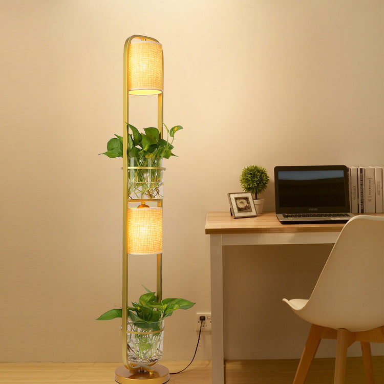 Modern floor lamp with a plant in a room with a desk and chair.