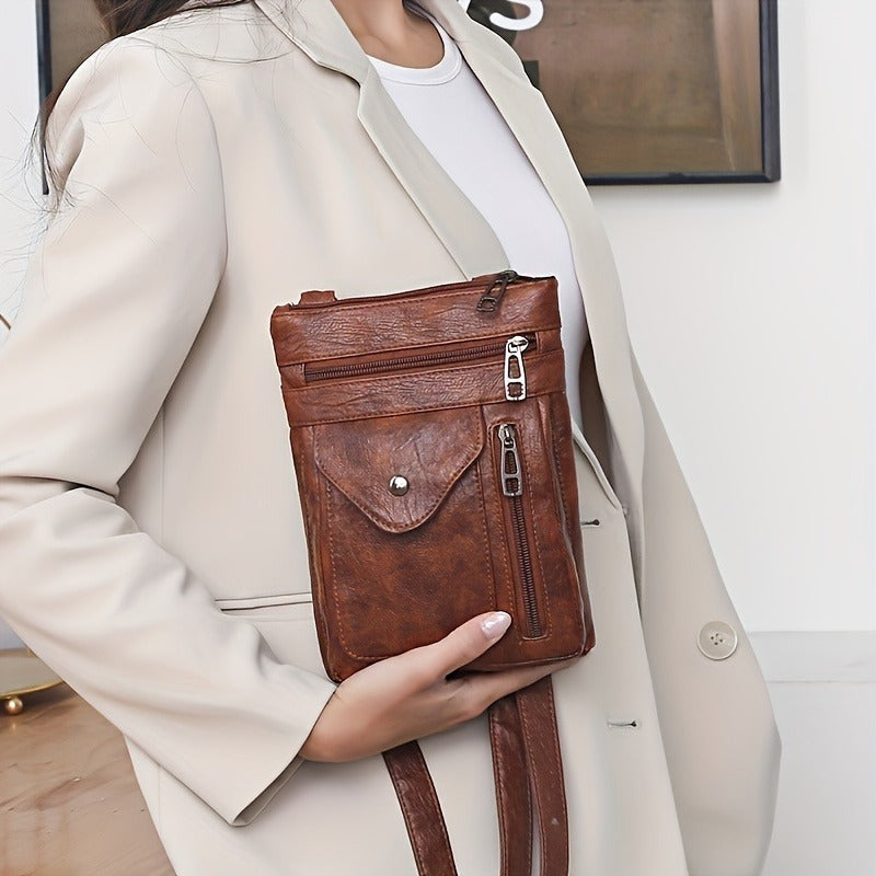 Person holding a brown leather crossbody bag against a neutral background