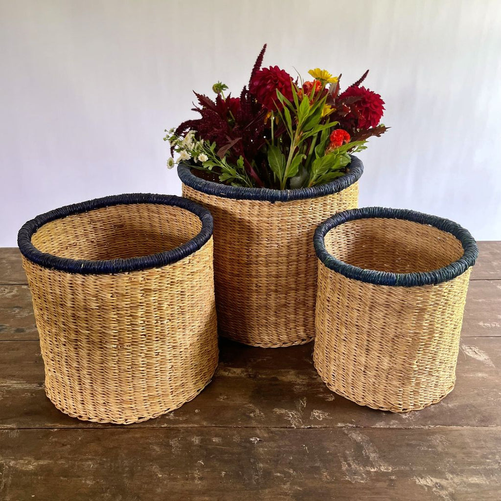Three woven baskets with blue rims on a wooden surface, one containing flowers.